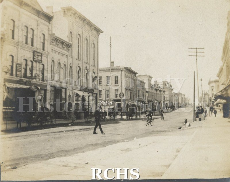 Black and white photograph of West Milwaukee St. before 1902. Phuekus Block on left-over street sign reads-"Public Library".