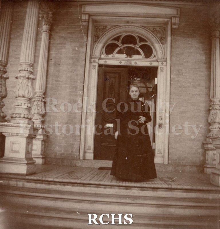 Black and white photograph of Mrs. Edward Tallman. She is standing on the steps of the Tallman House.