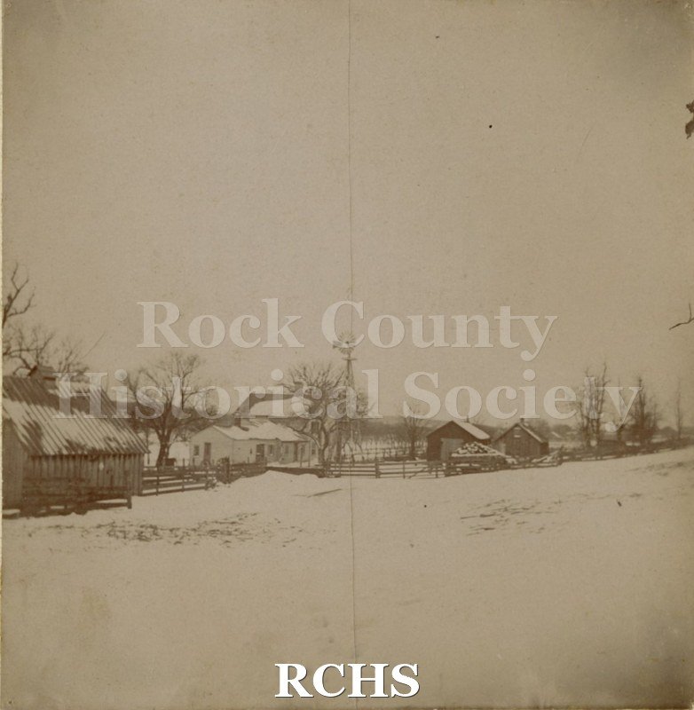 Sepia photo of Dole farm buildings? Shows a farm with snow on the ground. There is a house and many outbuildings as well as a windmill. .