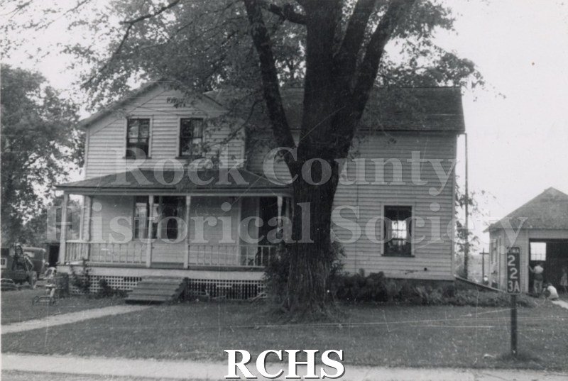 Black and white photograph of the farm home of Wallace and Mary Wheeler. This is a two story farmhouse with trees in front of it.