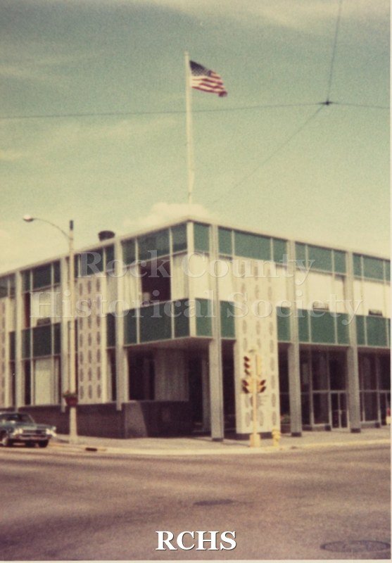 Color photo closeup of the front and side of the Rock County National Bank, showing decorative panels on each side of the front.