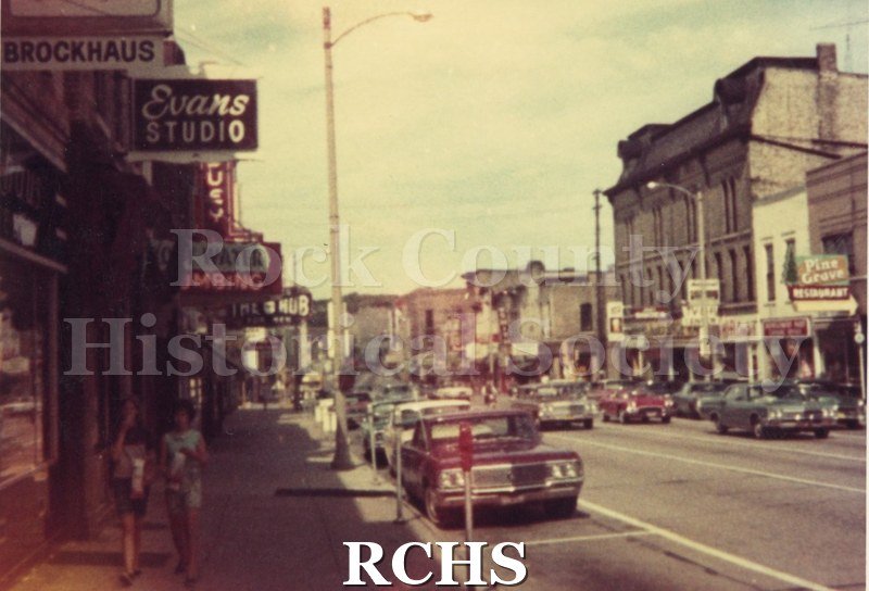 Color photo of West Milwaukee Street, Janesville. This shows the Pine Grove Restaurant on the right and Brockhaus Cleaners and Evans Studio on the left.