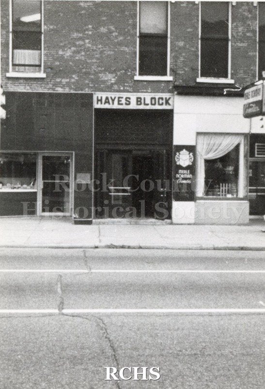 Black and white photograph of McLean's Jewelry and Merle Norman in the Hayes Block, Janesville, WI. Shows the side of the Hayes Block with store fronts.
