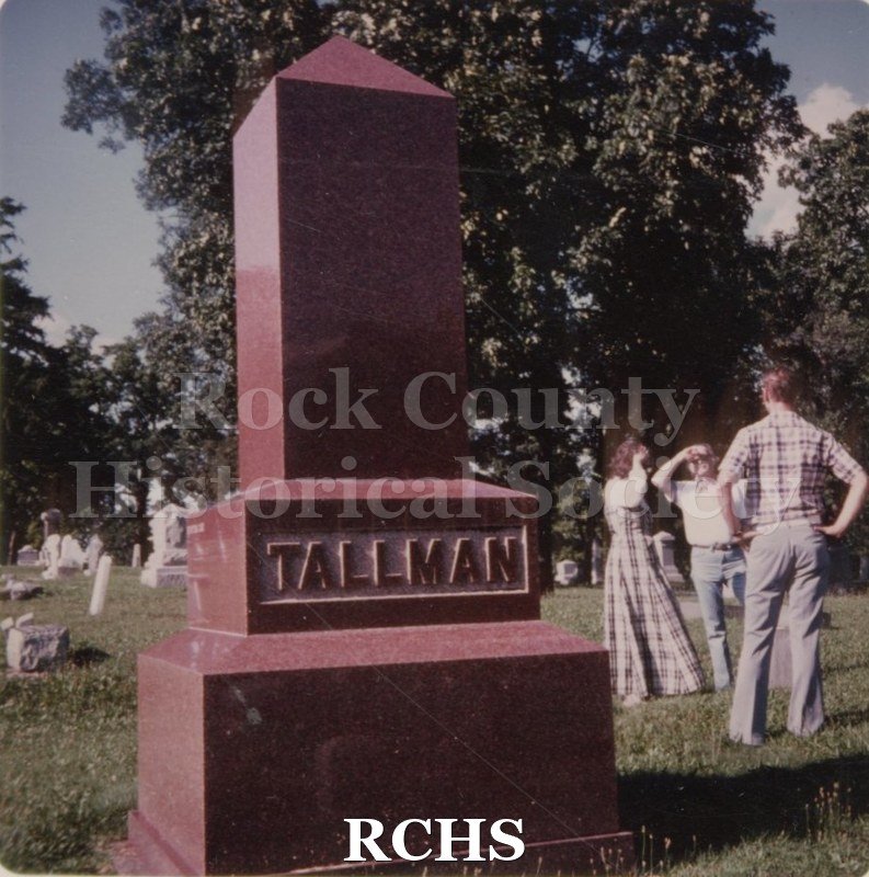 Color photo of the Tallman Monument. There are three people standing near the marker.