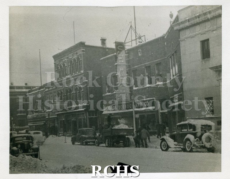 Black and white photogrpah of city street with snow on it. The Sears, Roebuck and Co. building is in the middle of the photograph.