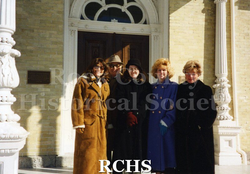 Color photo of five people, standing in front of Tallman House. One of the ladies pictured is Jackie Wood, others unidentified.