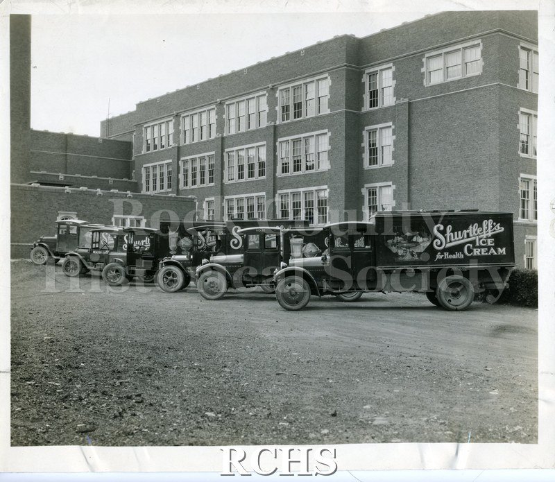 Black and white photograph of five Shurtleff's Ice Cream trucks in front of Janesville High School.