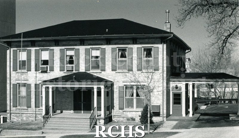 Black and white photograph of a two story house with six windows with shutters on the second floor and a porch in the middle of the first floor at 303 E.Court.