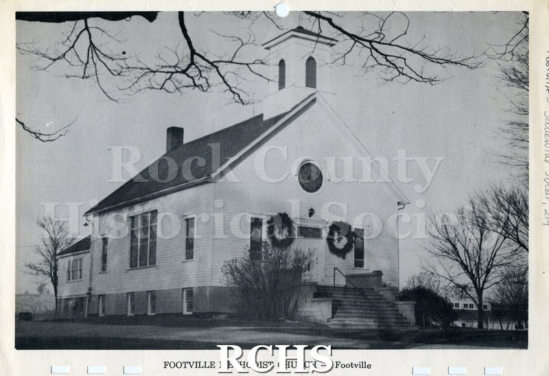 Black and white photograph of the Footville Methodist Church with evergreen wreaths on each side of the door and a bell tower.