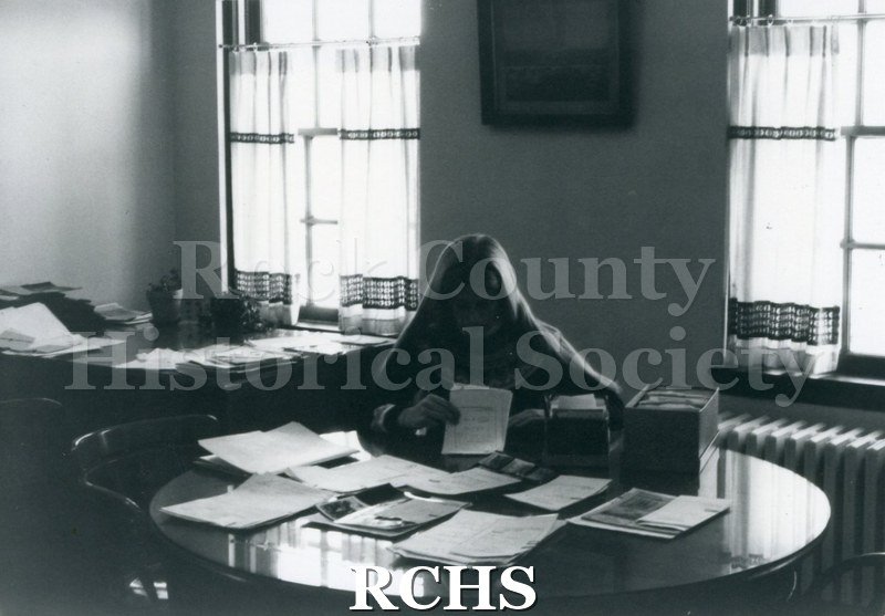 Black and white photograph of Sue Borges sitting at a desk with papers in front of her.