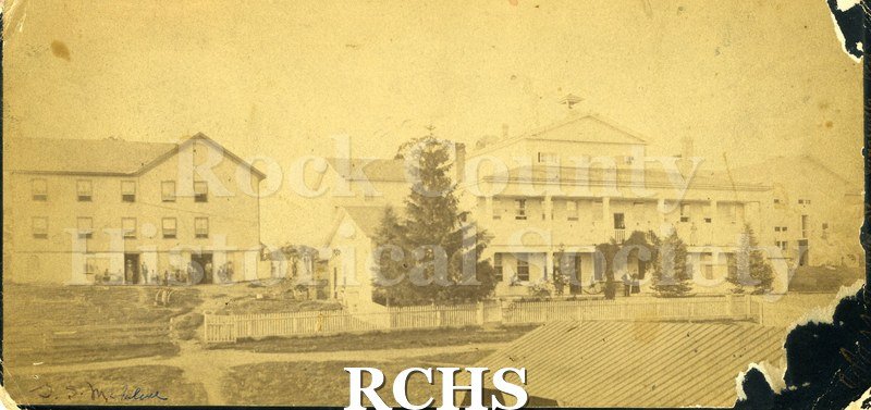 Black and white photograph of Rock Co. "Poor Farm". Shows a large three story building with several other buildings next to it.