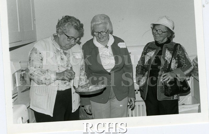 Black and white photograph of Jane H.Kohls, Mildred Rye and Esther Hodges looking at a pie.
