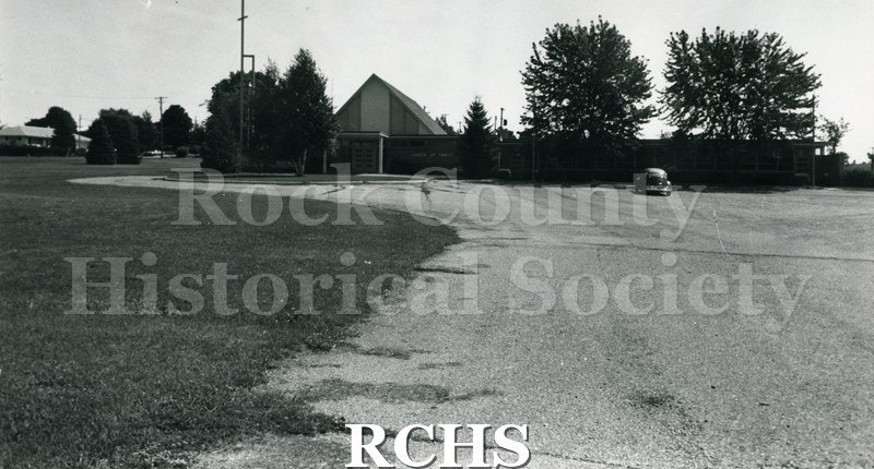 Black and white copy print of Church of Christ with one car in the parking lot. Photo is taken from a distance.