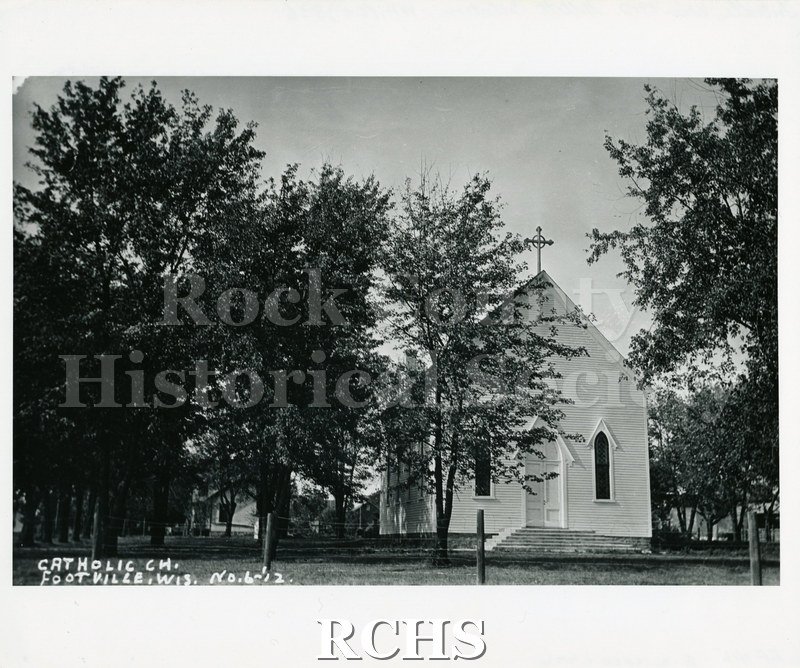Historic image of Black and white copy print of a small church with a cross on top. On bottom: "Catholic Ch. Footville, Wis. No. 6-'12.