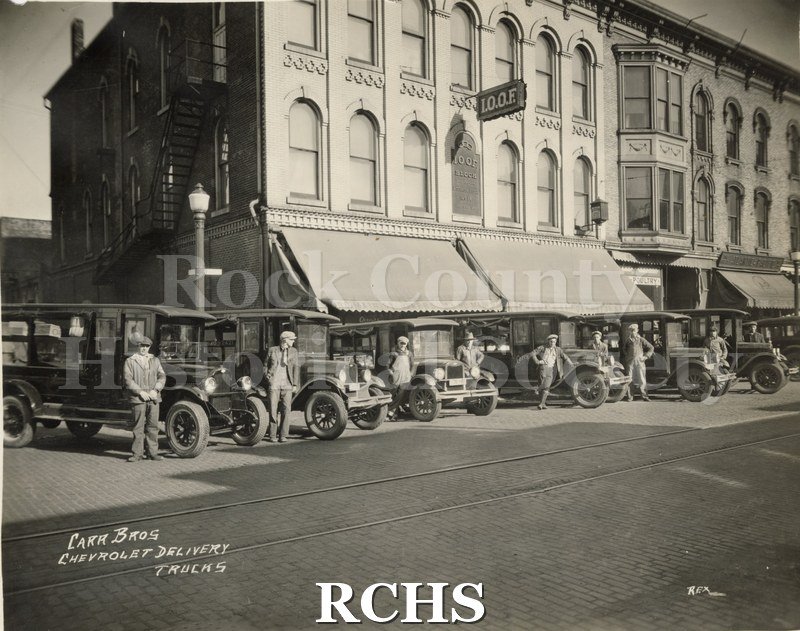 Black and white photograph of the exterior of Carr's grocery store with men standing beside the delivery trucks. On bottom: "Carr Bros Chevrolet Delivery Trucks".