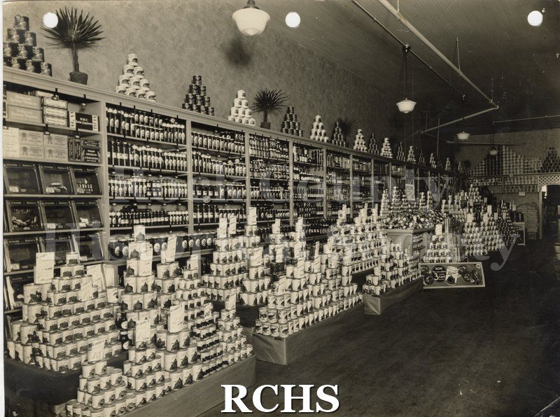 Black and white photograph of the interior of Carr's Grocery Store showing displays of canned goods in front of more products in cabinets.