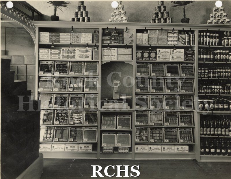 Black and white photograph of the iinterior of Carr's Grocery Store showing displays of canned goods in cabinets.