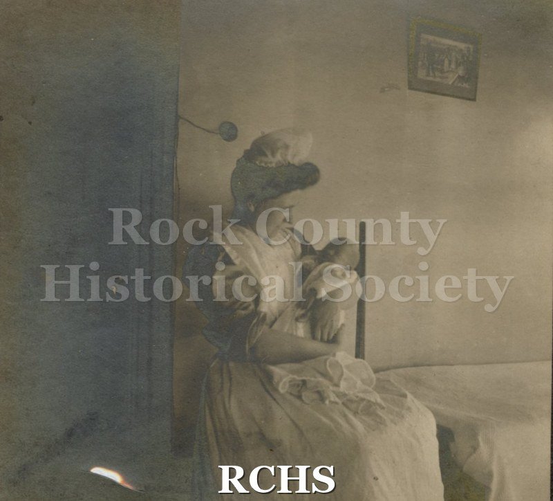 Black and white photograph of Minnie Tews, a nurse, sitting in a chair, holding a baby.