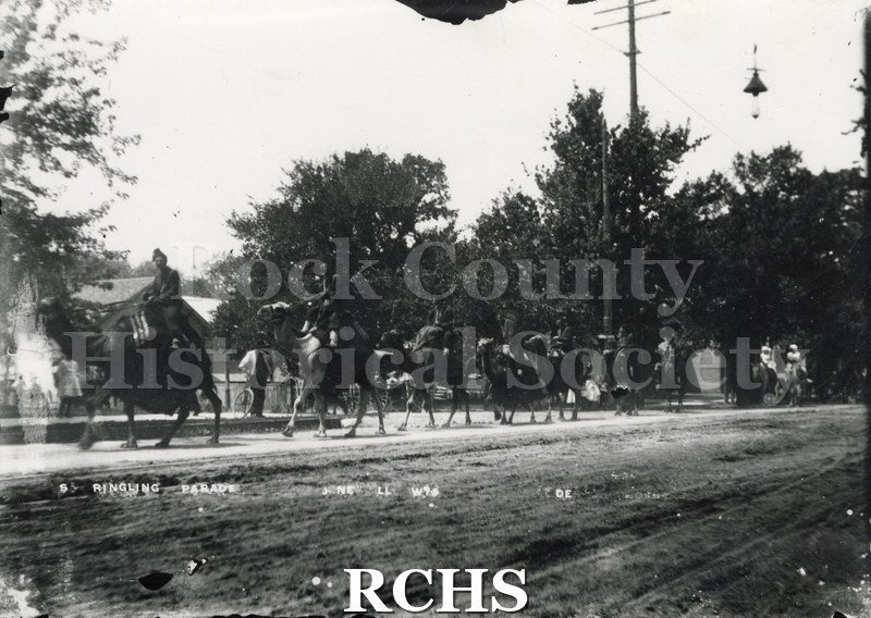 Black and white photograph of Ringling Circus Parade. Camels with riders are moving along the street. On photo: "S Ringling Parade, Janesville, Wis" GP1Neg.