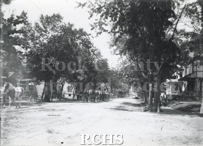 Black and white photograph of Ringling Circus Parade. A circus wagon pulled by six horses is moving along the street.