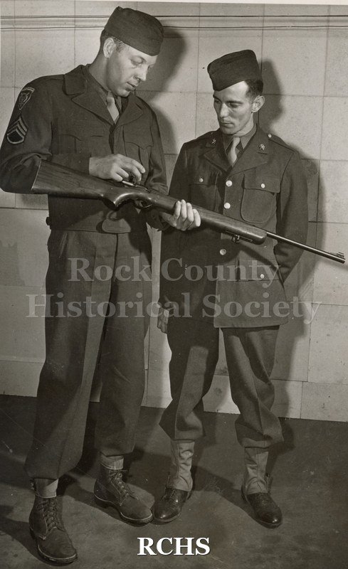 Black and white photograph of Sgt. Bienash and John Higgins examining a rifle.