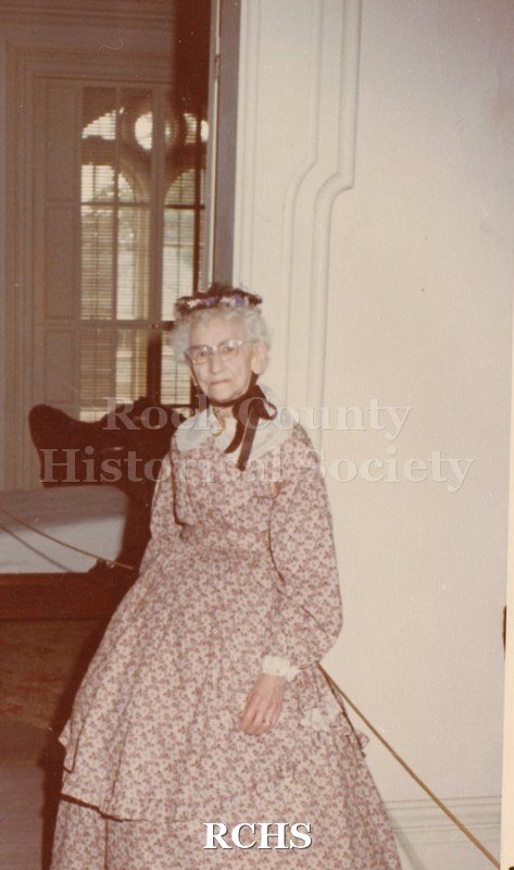 Color photo of Inez Smith wearing a period dress standing near a doorway in the Tallman House.