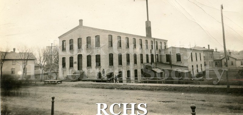 Black and white photograph of the Lewis Knitting Co. Shows a two story building with a large chimney on top.
