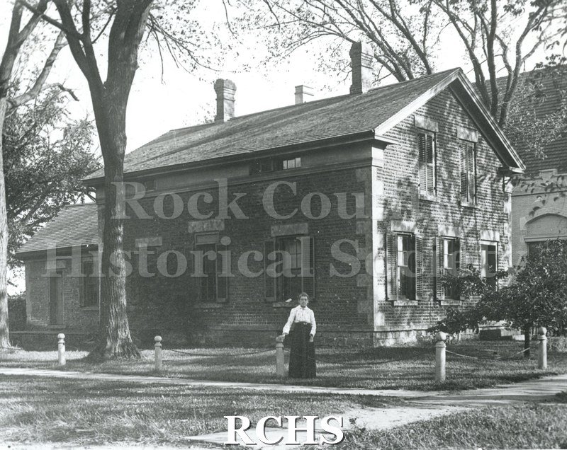 Black and white photograph of Rasey House, 517 Prospect St., Beloit, WI. It is a two story house with a woman standing in front of it.
