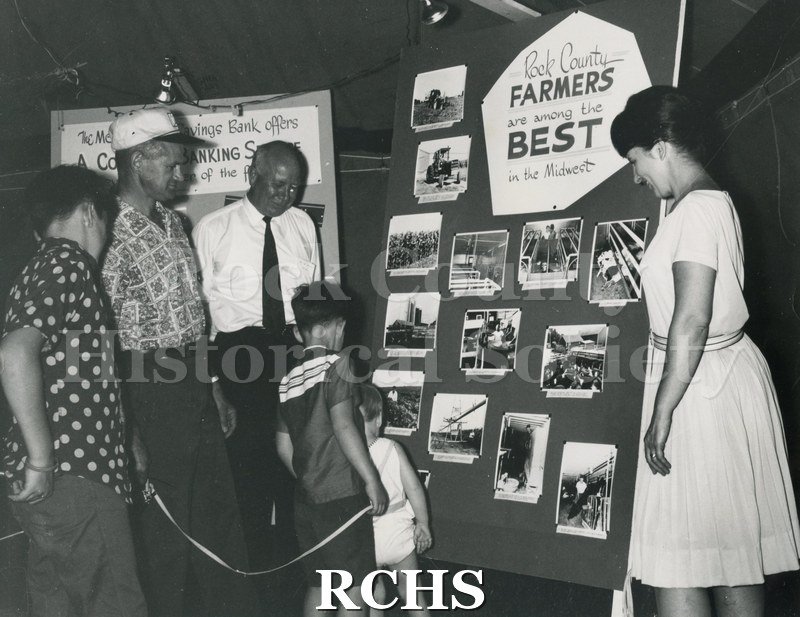 Black and white photograph of the M & S Rest Tent at 4-H Fair exhibit. Shows a family looking at an exhibit entitled "Rock County Farmers are among the Best in the.
