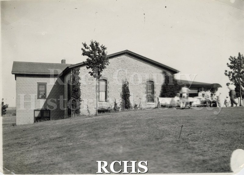 Black and white photograph of the Janesville Country Club. Shows a brick building with people golfing in the foreground.