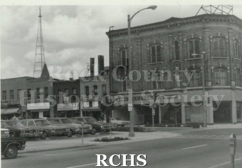 Black and white photograph of the front of an unidentified three story building on a corner.