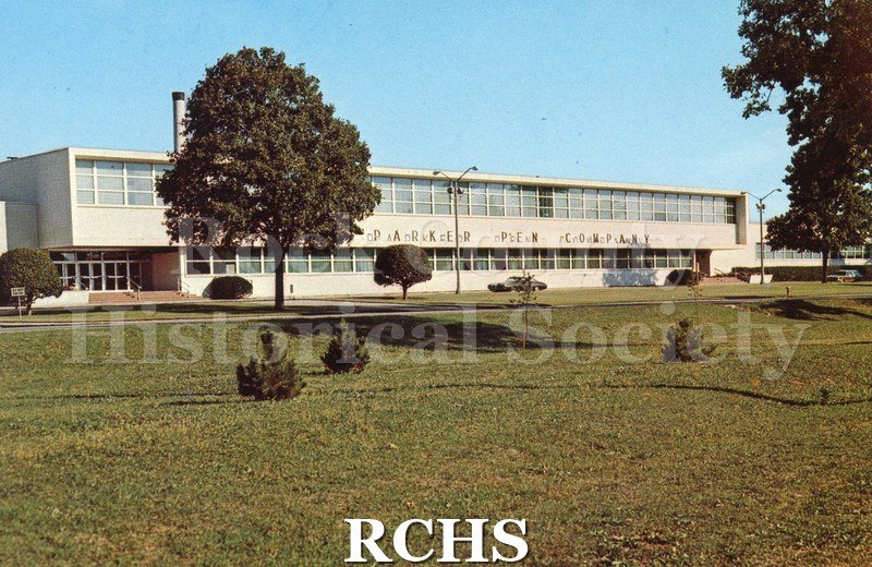 Postcard of Parker Pen Company Building with 2 cars in front. Tree on left and 1 on right, some bushes and saplings.