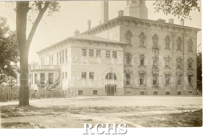 Black and white postcard of building with trees, grass and sidewalk in foreground. Building is 3 1/2 stories, Italiante style.