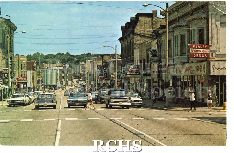 Postcard of Janesville Street Scene. Cars, storefronts and people visible. Reverse has description of Janesville and mentions Parker Pen and Chevrolet.