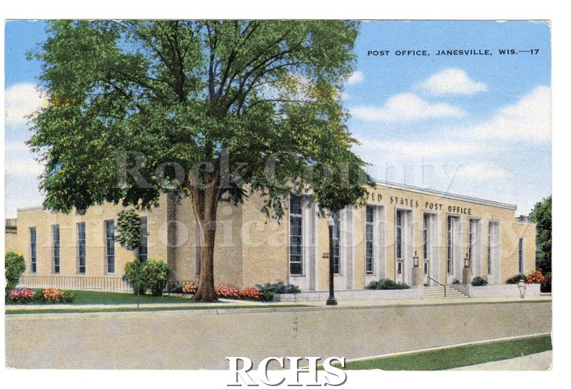 Postcard of United States Post Office with large tree on left, flowers around building. Woman visible in right corner.