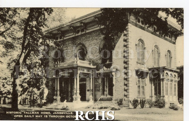 Black and white photograph of Lincoln Tallman House showing the front porch and conservatory sides. Shrubs along front of house, trees in front and back.