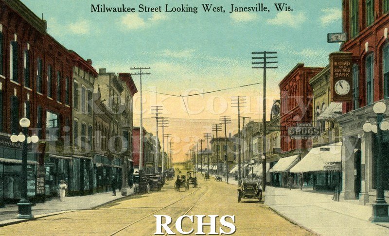 Postcard. Tinted image of Milwaukee Street looking west in downtown Janesville. No postmark. Brief message written in ink: "Two Clara Olson, From Edward W. Hoague.".