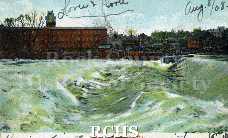 Postcard. Tinted image of the upper dam on the Rock River in Janesville with the woolen mill in the background.