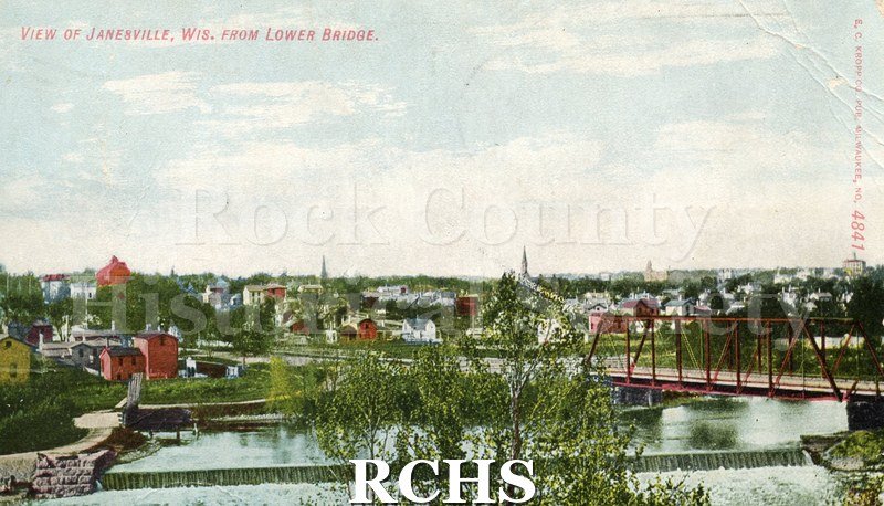 Postcard. Tinted image of a view of Janesville from a lower bridge. Postmarked 7 December 1908 and addressed Ida Krahmer of Beloit.