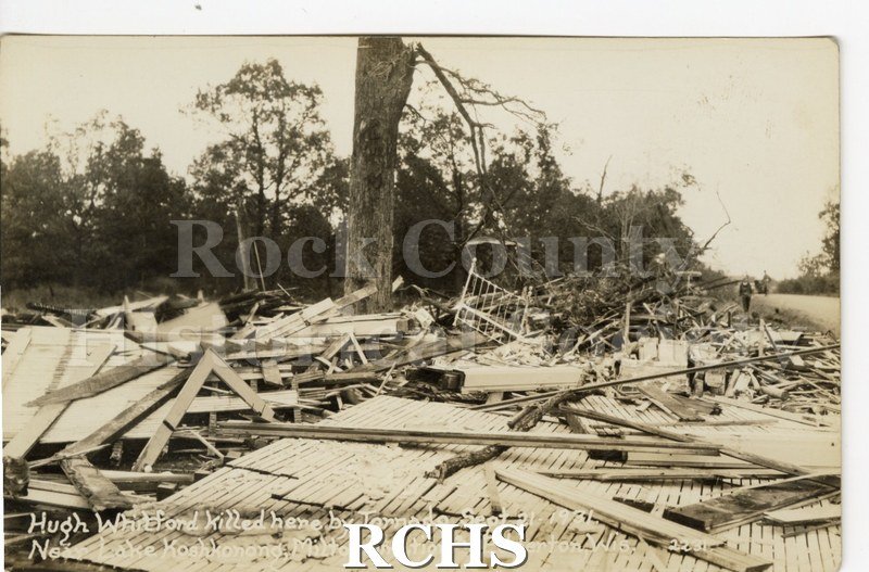3-1/2" x 5-1/2" glossy picture postcard showing debris left from tornado. There is a man standing in the background on the right.