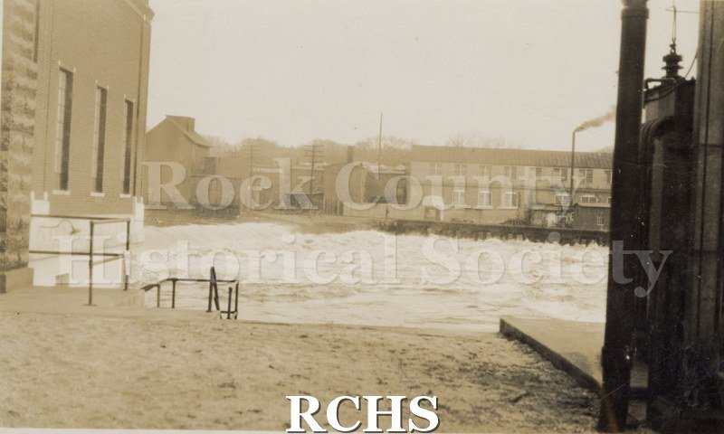 Historic image of Rock River at flood stage. There are buildings in the background.