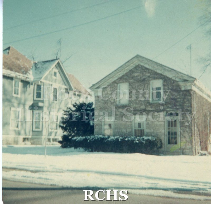 Color photo of 340 Euclid, Beloit, WI. Shows a two-story stone house with evergreen shrubs in front.