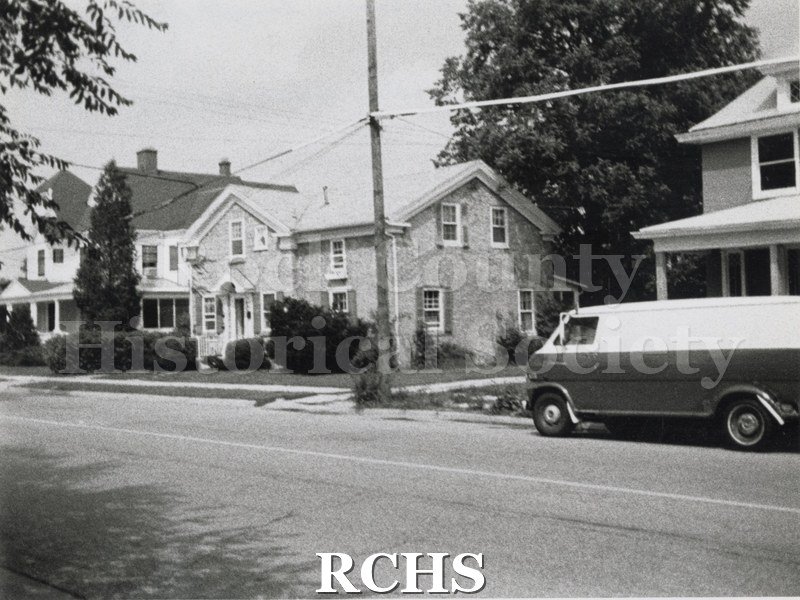 Historic image of Carson House is a two story stone house. There are other houses on the left and right. A van is parked on the street on the right side.