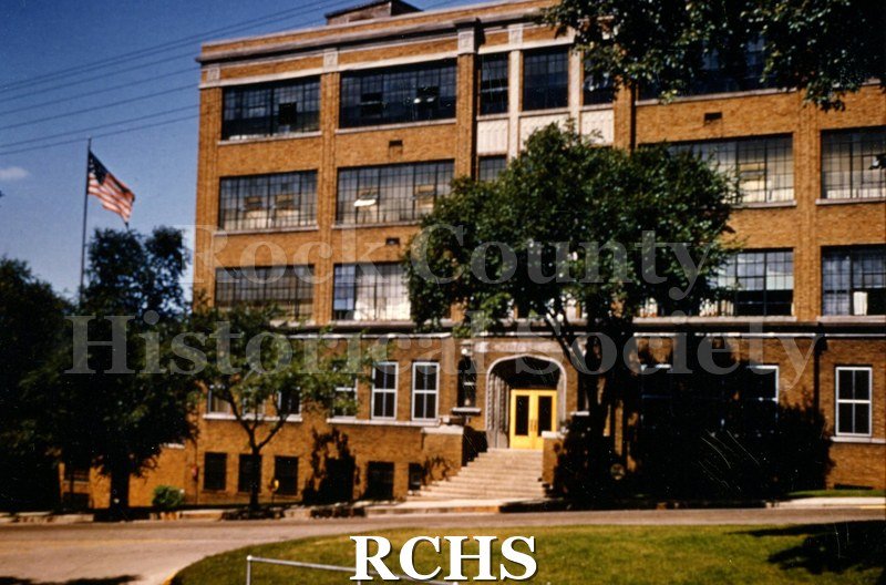 Color photo of Parker Pen building. Shows flag flying on a pole and trees in the front.
