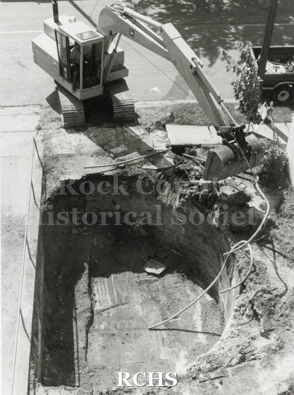 Black and white photograph of a machine with a bucket in front working on an excavation.