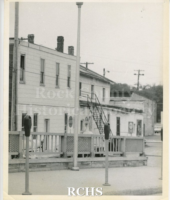 Black and white photograph of Connell's Marine. Shows the back of a two story building. There are two parking meters in front of the building.