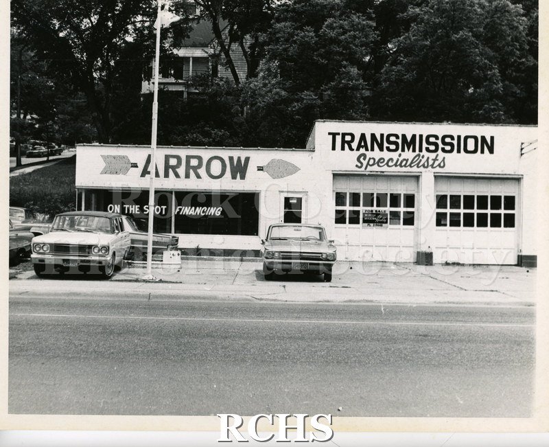 Black and white photograph of a garage with "Arrow" and "Transmission Specialists" on the top part and in the window is a sign: "On the spot financing".