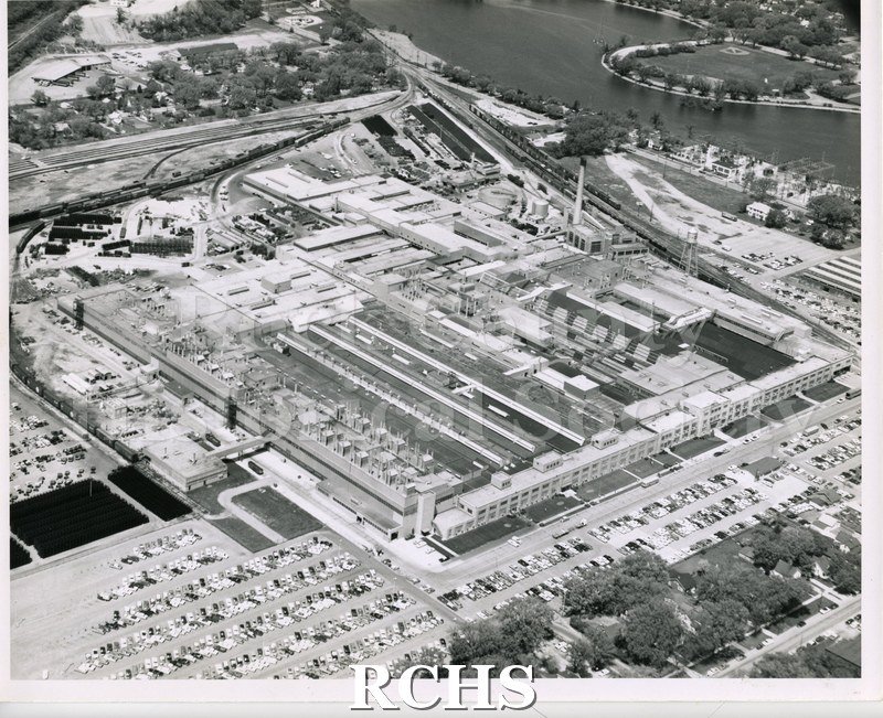 Black and white aerial photograph of the General Motors Plant. Shows buildings and cars parked as well as the river in the background.