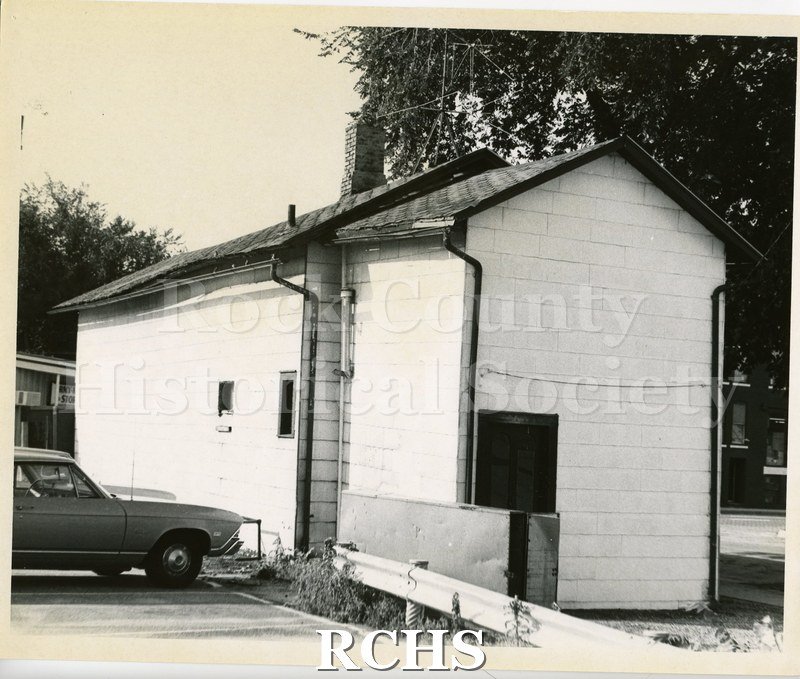 Black and white photograph of the 500 block of W. Milwaukee Street. Shows a one story building with a car in front.