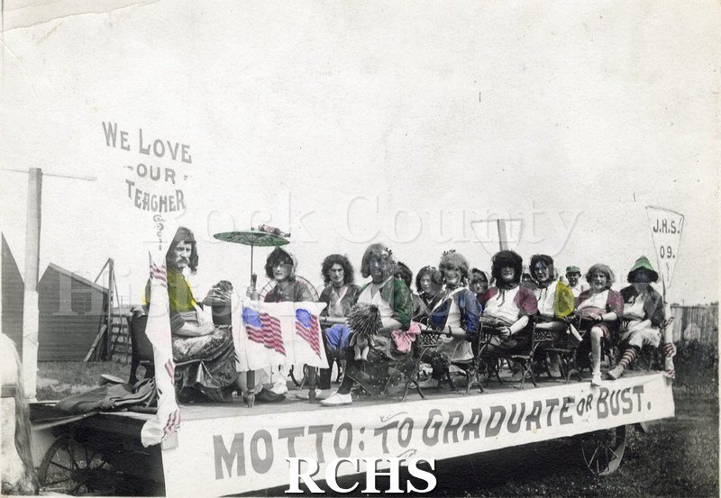Historic image of Nonesuch Brothers Circus parade float with 10-15 men dressed as females seated as in a classroom taught by a teacher.